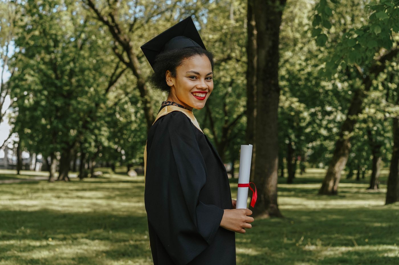 Recent graduate holding her diploma in a park